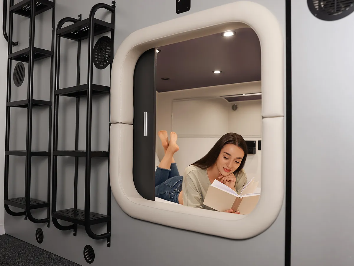 Young woman reading book in capsule of pod hostel