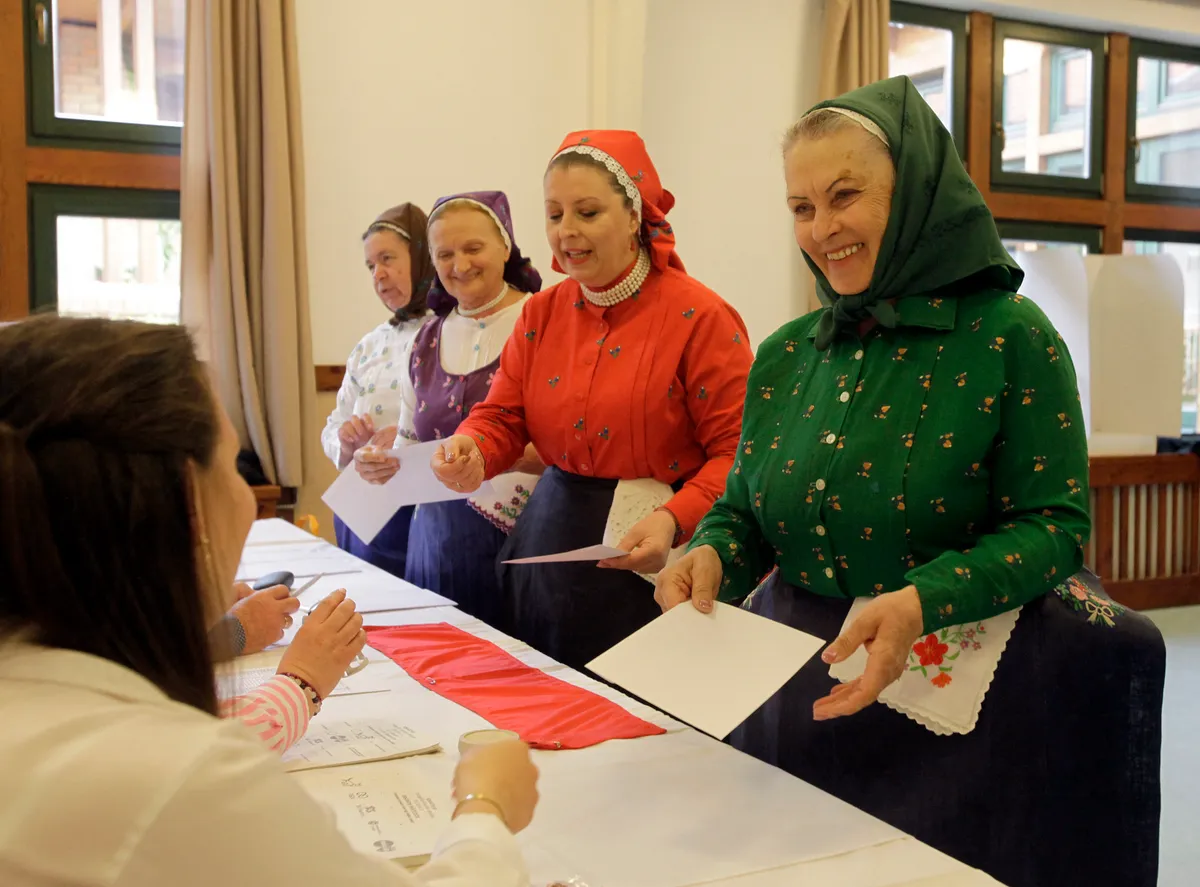 Women in traditional Hungarian dresses get their ballot papers at a polling station in a nursery school in Veresegyhaz, some 30km east of Budapest, on April 12, 2026, during the general election in Hungary. The vote could end Hungarian Prime Minister Viktor Orban's 16-year stint in power as the EU's longest serving current leader and a self-decribed "thorn" in the bloc's side. (Photo by Peter Kohalmi / AFP)
