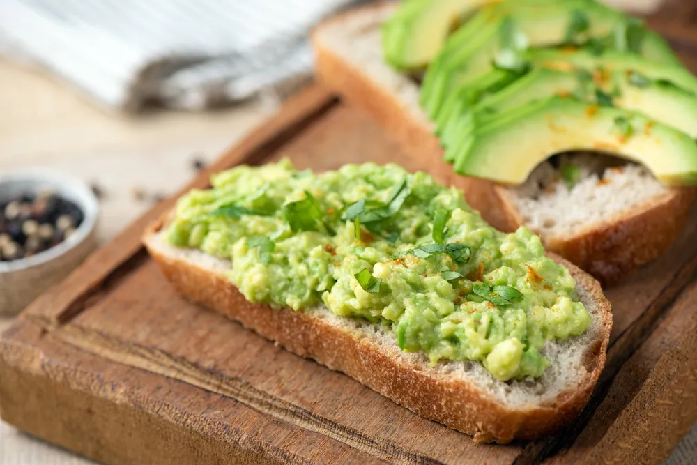 Bread toast with mashed avocado and chopped parsley on a wooden serving board, closeup view