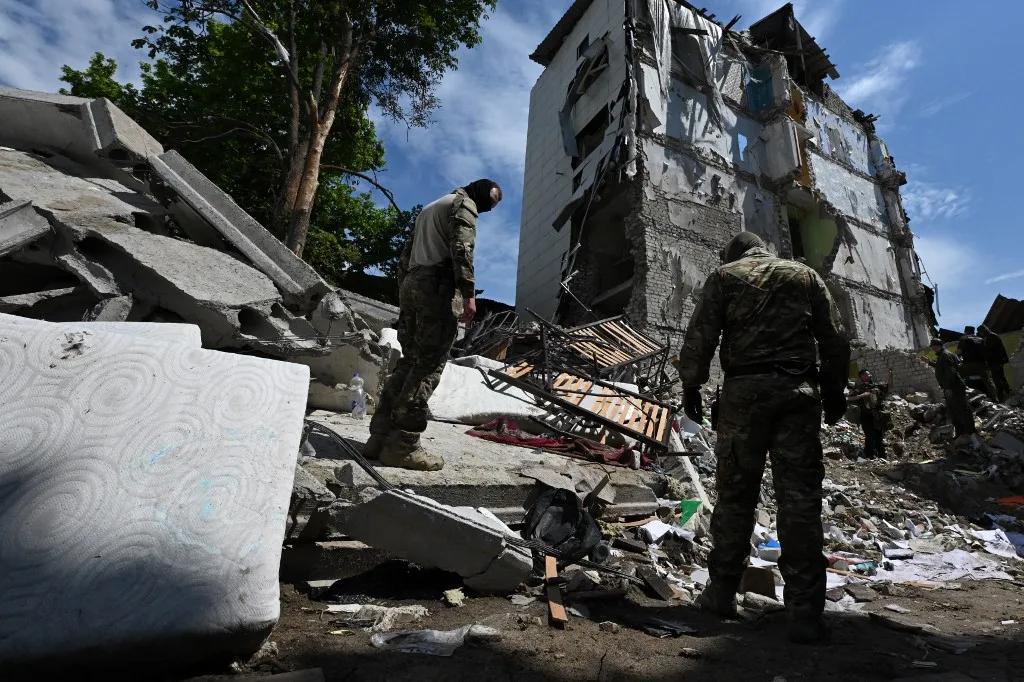 Orosz-ukrán háború: Moszkva megtorlást helyezett kilátásba Kijev ellen, a sztarobelszki kollégium megtámadása miatt - A group of men, including Russian investigators, are seen among rubble of what is presented by Russian authorities as the destroyed dormitory building of the Starobilsk professional college of the Luhansk Pedagogical University, following a drone attack in Starobilsk, Russian-controlled Ukraine, on May 24, 2026. Russia states that 21 students at the college were killed in a Ukrainian strike launched overnight on Thursday to Friday. Ukraine had denied targeting civilians, insisting it had hit a Russian drone unit stationed in the Starobilsk area. (Photo by Igor IVANKO / AFP)