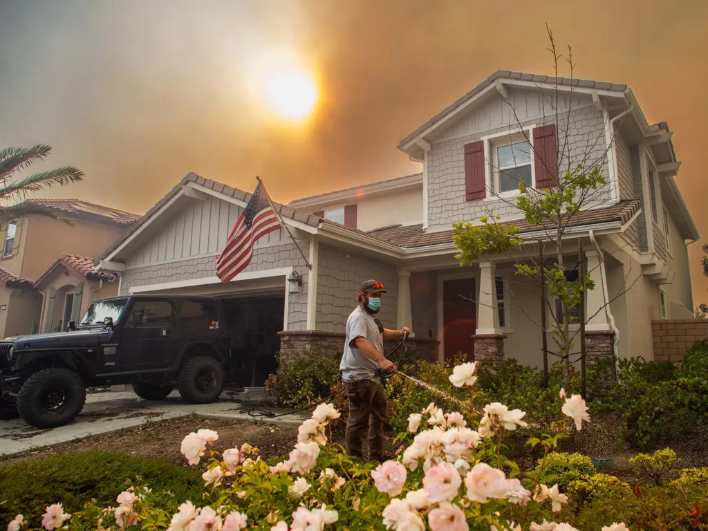 Erdőtűz, Kalifornia, ErdőtűzKalifornia, 2026.05.19., A resident uses a garden hose to watering his front yard plants as the Sandy Fire burns in the hills close to a residential area in Simi Valley, California, on May 18, 2026. About 24,000 people in Simi
