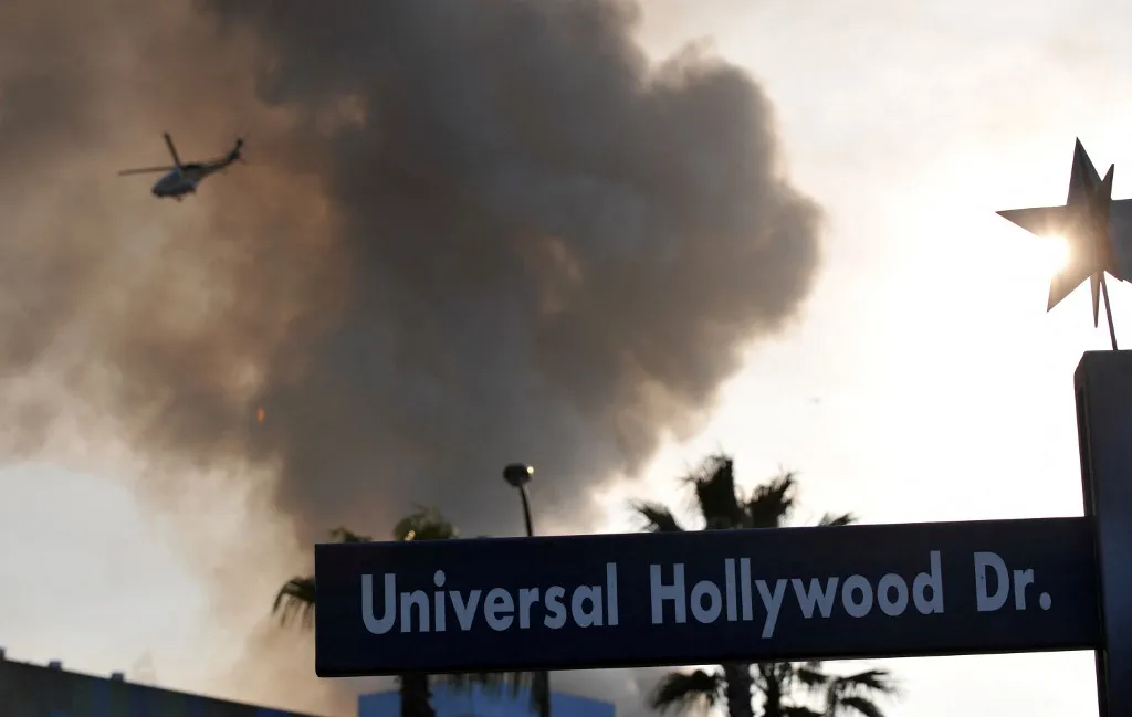 A helicopter flies over burning structures at Universal Studios, in Universal City, California, on June 01, 2008. More than 100 firefighters were battling a huge fire early Sunday on the backlot at Universal, destroying several movie sets. Universal Studios is just north of Los Angeles and is an amusement park as well as a working movie and television studio. AFP PHOTO GABRIEL BOUYS (Photo by GABRIEL BOUYS / AFP)