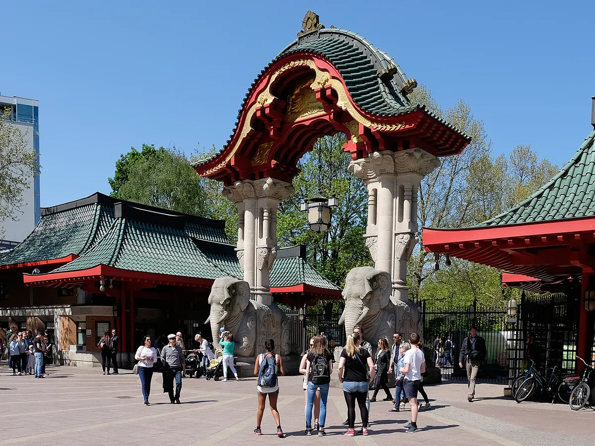 Berlin, Germany - May 05, 2016: Visitors gather at historic zoo entrance with ornate East Asian style gate and elephant column sculptures, ticket booths and spring foliage visible as families and tourists pass through plaza