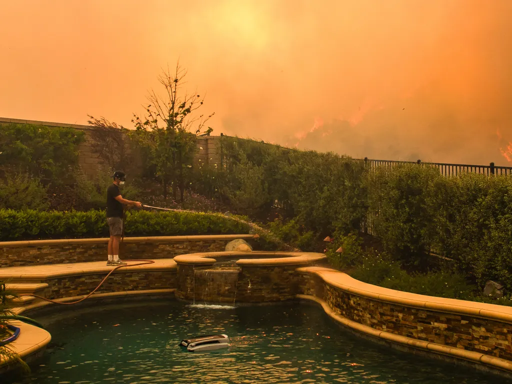 Erdőtűz, Kalifornia, ErdőtűzKalifornia, 2026.05.19., A resident uses a garden hose to watering his backyard as the Sandy Fire burns in the hills close to a residential area in Simi Valley, California, on May 18, 2026. About 24,000 people in Simi Valley,