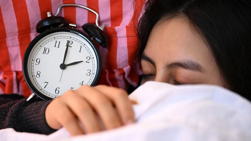 alvás ILLUSTRATION - 19 March 2026, Berlin: A sleeping woman lies in bed with an alarm clock. Daylight saving time begins in Germany on 29.03.2026. Photo: Elisa Schu/dpa (Photo by Elisa Schu / dpa Picture-Alliance via AFP)