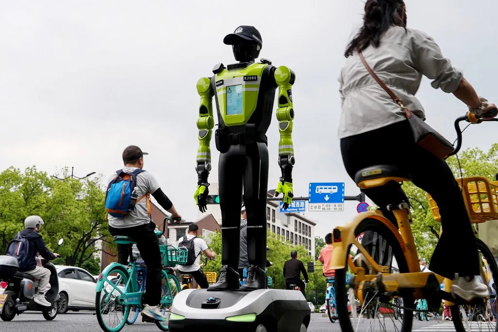 Robotrendőrök irányítják a forgalmat KínábanPeople cycle past a humanoid robot police officer in Hangzhou, in Chinas eastern Zhejiang province on May 3, 2026 on the third day of a five-day national May Day holiday. The tech hub's traffic police deployed 15 humanoid robots in total to bolster their ranks on May 1. (Photo by Agatha CANTRILL / AFP)