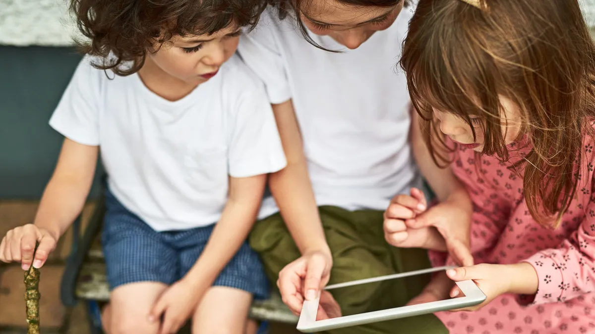 Engaged in a whole wide world online. three adorable little children using a digital tablet while sitting on a bench outdoors.