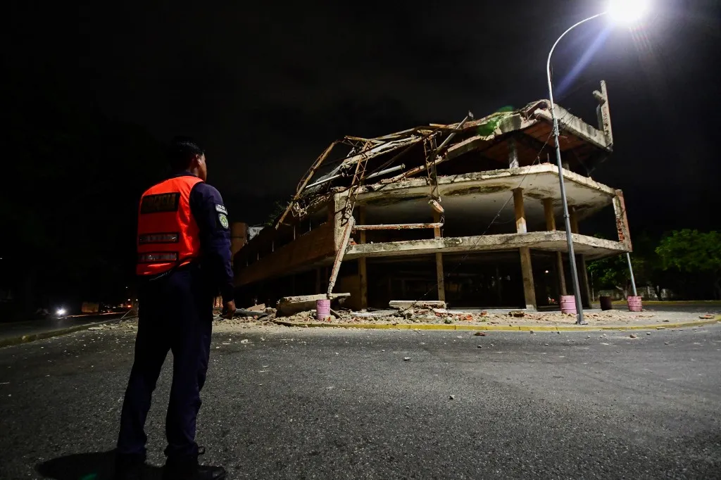 A Venezuelan municipal police officer stands next to a collapsed building following an earthquake in Valencia, Venezuela on June 24, 2026. Two earthquakes of magnitude 7.2 and 7.5 struck the same area of Venezuela on the evening of June 24, causing buildings to collapse, according to the United States Geological Survey (USGS) and AFP journalists. The quakes drove residents of the capital, Caracas, into the streets. (Photo by Jacinto OLIVEROS / AFP)