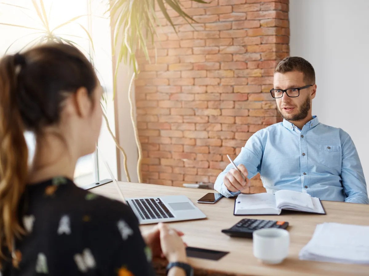 Close up of mature bearded company director in glasses sitting in office with dark-haired girl in front of him on job interview. Man asking women about work experience