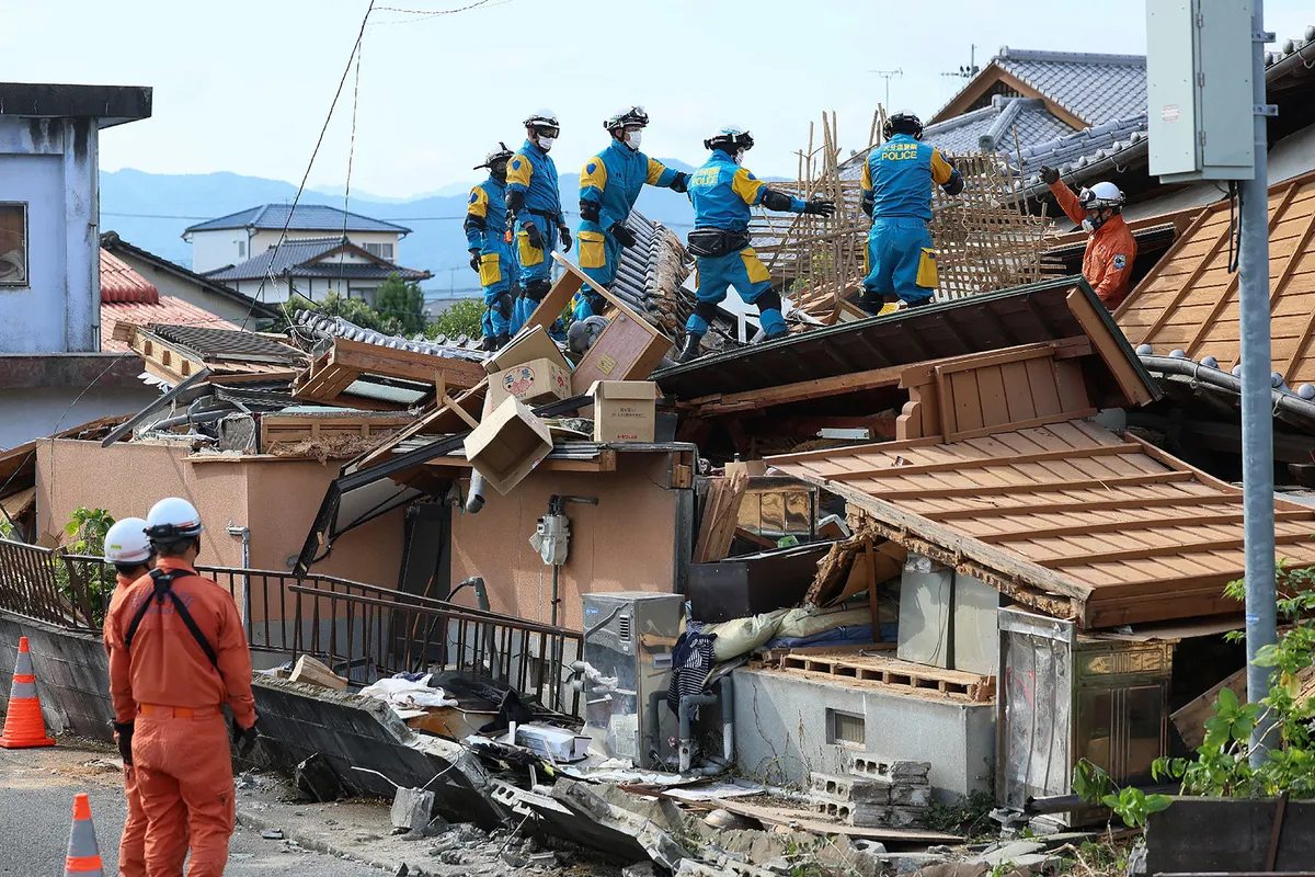 Rescue officials work at the site of a house, which was damaged in the July 28 earthquake, in Yatsushiro, Kumamoto prefecture on July 30, 2026. Up to 23 people were feared dead on July 30 after a major earthquake in Japan, with four bodies now pulled out from the tangled wreckage of a shopping mall devastated by a suspected gas explosion. (Photo by JIJI Press / AFP) / Japan OUT