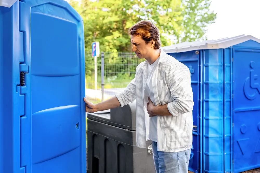 Férfi egy mobil wc előtt fesztiválbetegségekből adódó rosszullét miatt