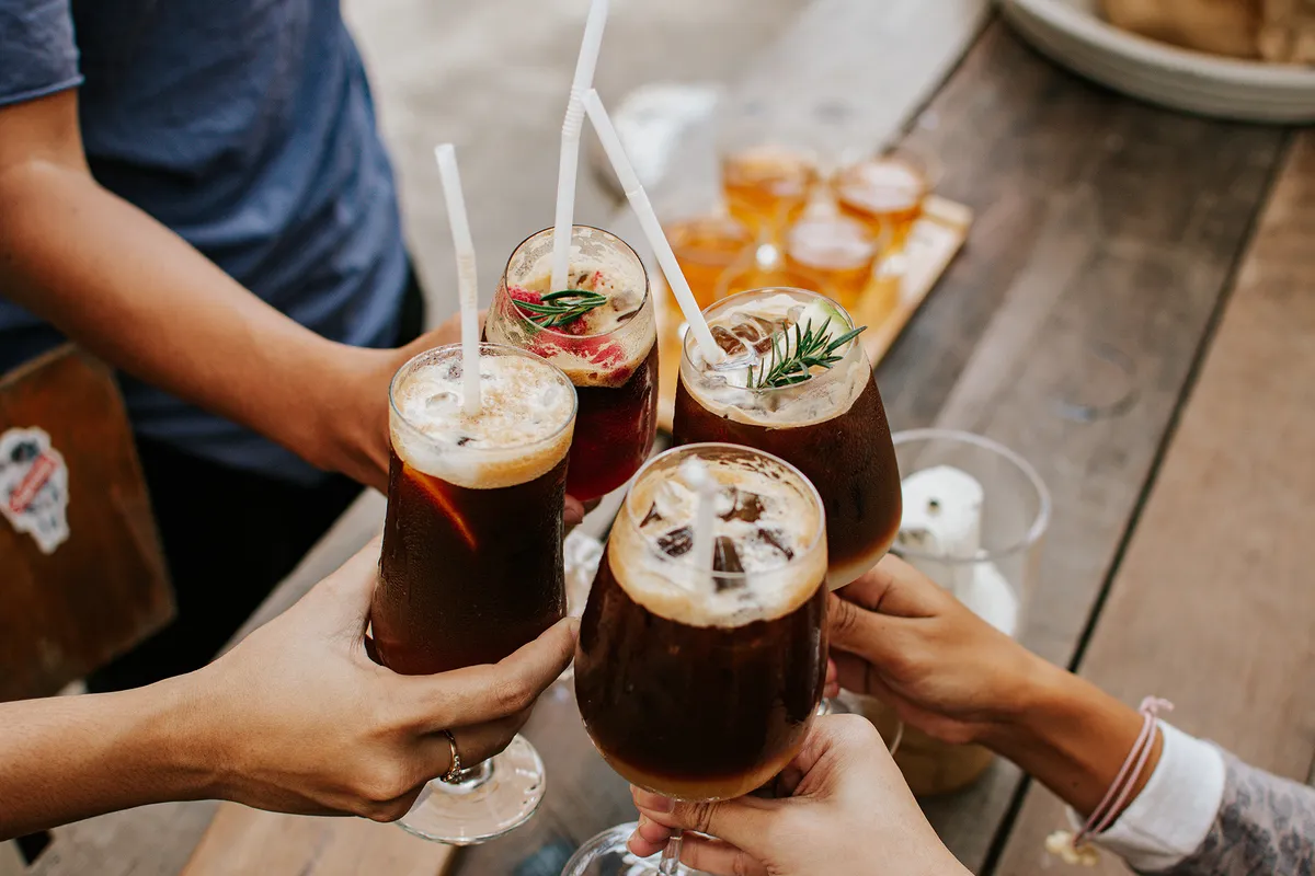 Négy ember (csak a kezük) koccint cold brew kávékoktélokkal.