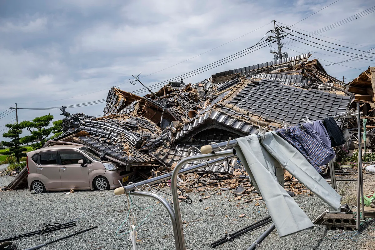 A house is seen collapsed onto a car in Hikawa, Kumamoto Prefecture on July 30, 2026 after an earthquake struck the area. The Aeon shopping mall in Kumamoto had only reopened in June, gleaming, stronger and safer thanks to the latest renovations following earthquakes in 2016, promising a place where generations could "share smiles". But despite extensive reinforcement works on the facility that suffered severe damage a decade ago, a blast triggered by a fresh quake on July 28, in the southwestern Japanese region has left it in ruins. (Photo by Yuichi YAMAZAKI / AFP)