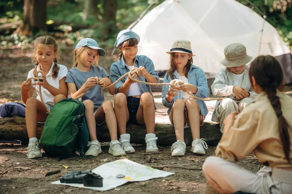 Survival tips, sitting at camp. Woman is doing tour for group of kids in the forest.