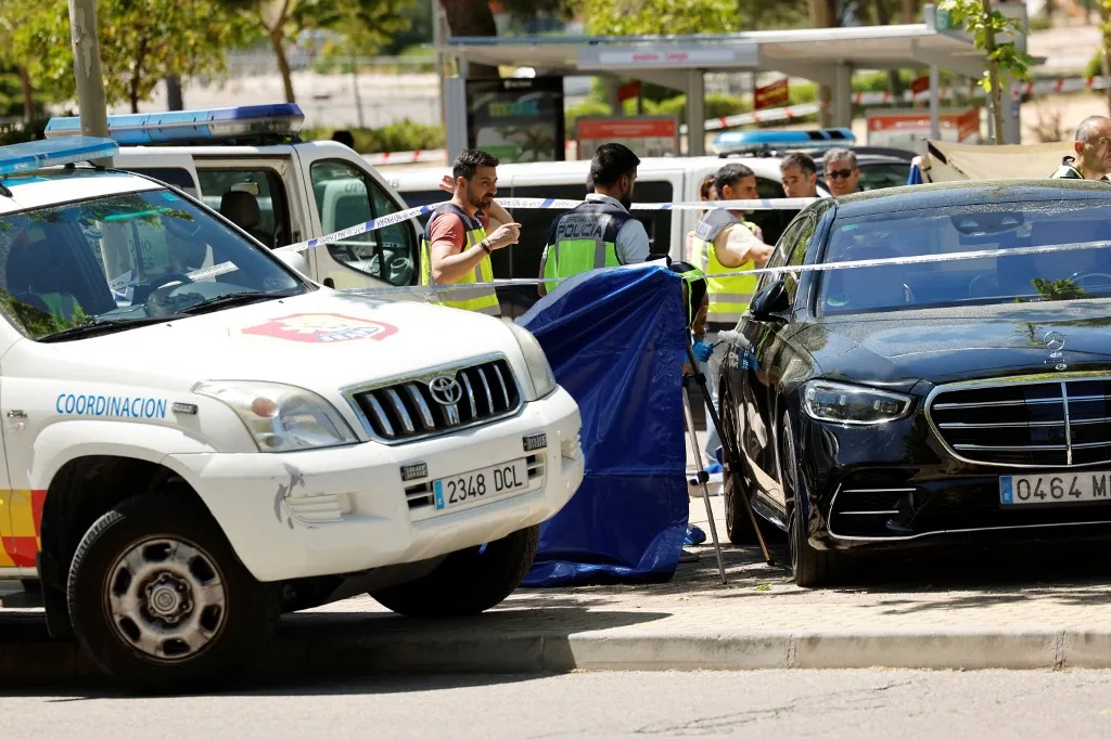 Kiadták Spanyolországnak az ukrán politikus feltételezett gyilkosát (A képen a tavaly májusban történt merénylet színhelye), Police officers work near the body (behind blue curtain) of late ex-Ukraine MP Andrey (Andriy) Portnov, and his car (R), after he was shot dead in front of his children school in Pozuelo de Alarcon, near Madrid, on May 21, 2025. A US-sanctioned ex-Ukrainian MP and aide to the country's former pro-Russian president, Andrey (Andriy) Portnov, has been shot dead in Pozuelo de Alarcon, near Madrid, according to police source, AFP reports on May 21, 2025. (Photo by OSCAR DEL POZO / AFP)