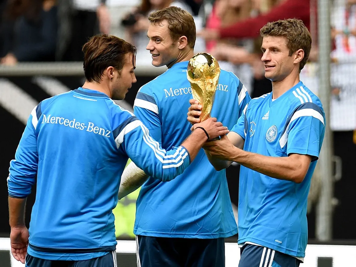 Germany's forward Thomas Mueller (R), Germany's forward Mario Goetze (L) and goolkeeper Manuel Neuer present the World Cup trophy to fans during a public training session of the German national football team in Duesseldorf, Germany on September 1, 2014. Germany's squad prepares for the upcoming friendly game against Argentina on September 3, 2014 in Duesseldorf. AFP PHOTO / PATRIK STOLLARZ (Photo by PATRIK STOLLARZ / AFP)