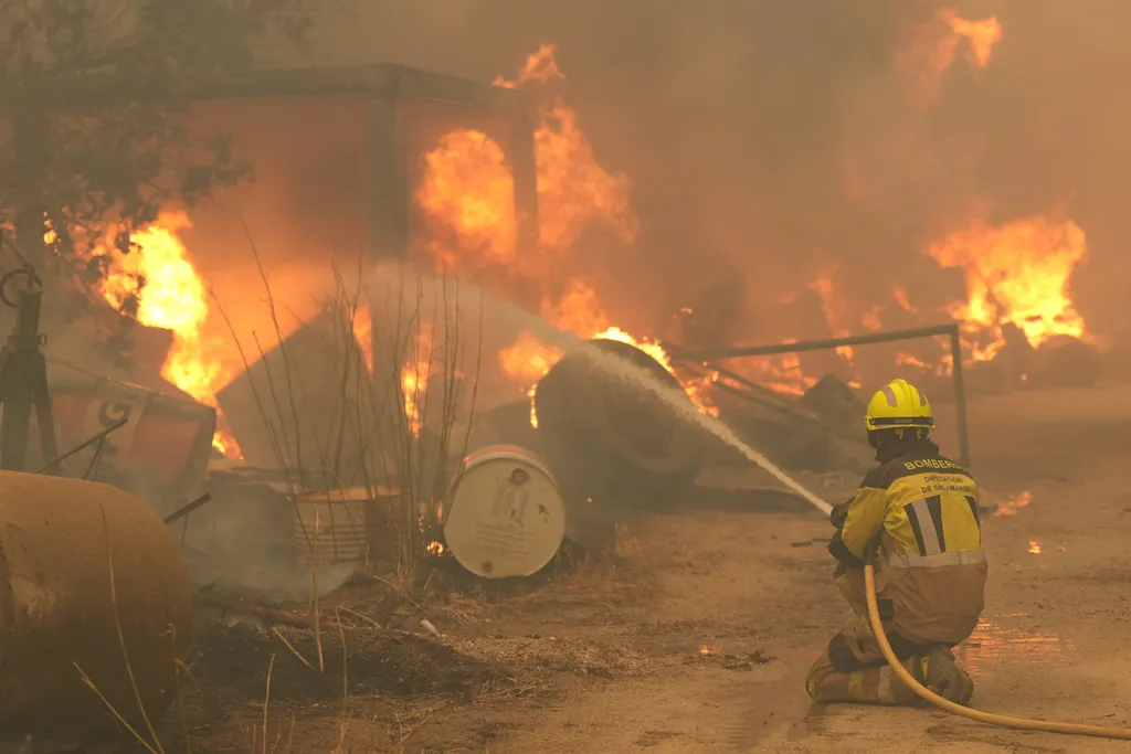 A firefighter waters burning tires and barrels while battling a wildfire in Cebreros area, near Avila, 80 kms west of Madrid on July 24, 2026. The worst wildfires in the Madrid region's history rage west of the Spanish capital, forcing authorities to evac