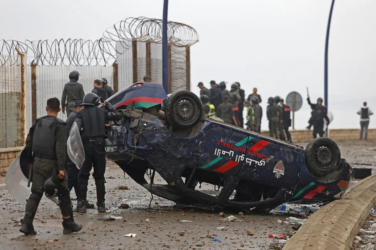 Members of Moroccan security forces gather next to an overturned damaged vehicle at the site of clashes near Fnideq, on the Morocco-Spain border, on July 31, 2026. Thousands of migrants crossed overnight from Morocco into Spain's north Africa's Ceuta enclave, a police source said on July 31, as Prime Minister Pedro Sanchez was set to arrive to manage the latest migrant crisis on the border. (Photo by Abdel Majid BZIOUAT / AFP)