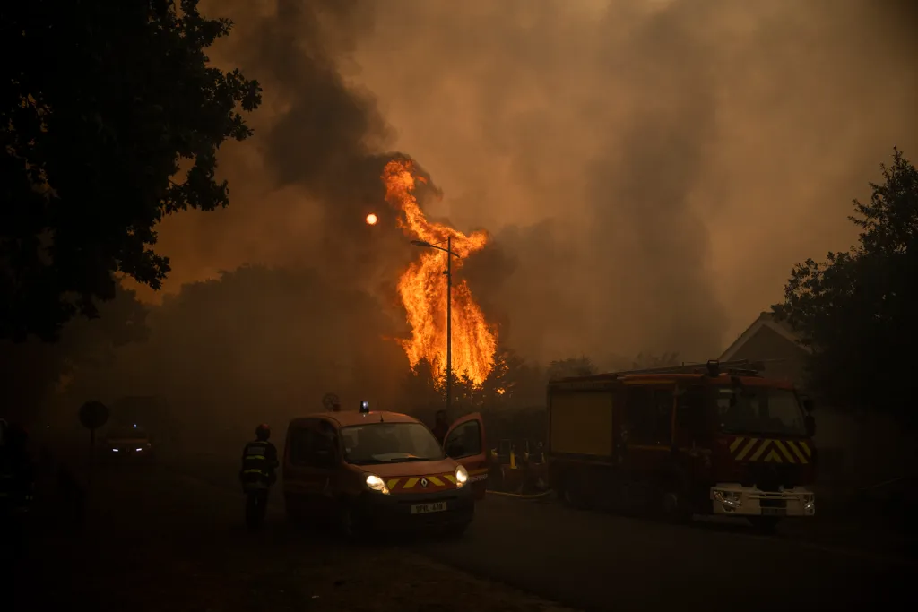 Firefighters operate next to flames at a residential area during a wildfire near Lege Cap Ferret, southwestern France on July 23, 2026. The fire, which broke out in Saumos on July 22 around midday, quickly moved toward Lège-Cap-Ferret, spreading very rapi