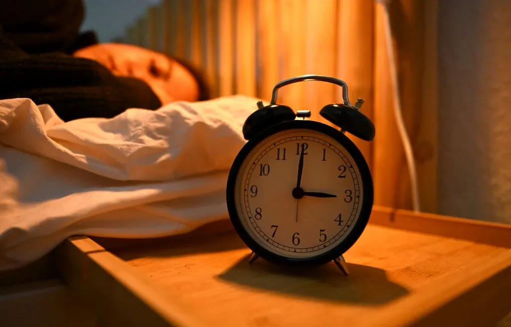 ILLUSTRATION - 19 March 2026, Berlin: An alarm clock stands next to a bed in which a woman is sleeping. Daylight saving time begins in Germany on 29.03.2026. Photo: Elisa Schu/dpa (Photo by Elisa Schu / dpa Picture-Alliance via AFP)