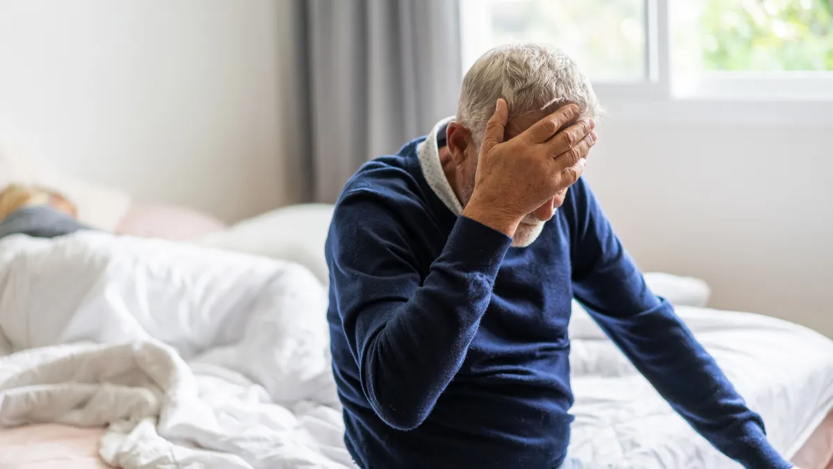 Alzheimer-kórral küzdő idős férfi az ágyon ülve, fejét a kezébe temetve