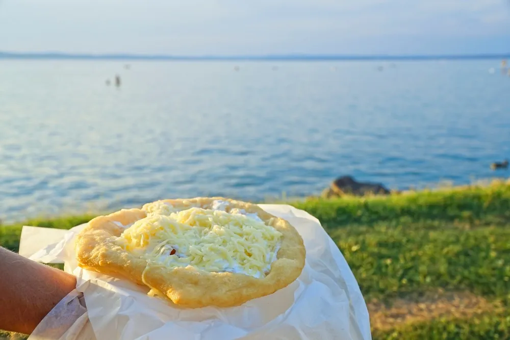 Balatoni lángos kézben tartva sajttal, tejföllel és fokhagymával