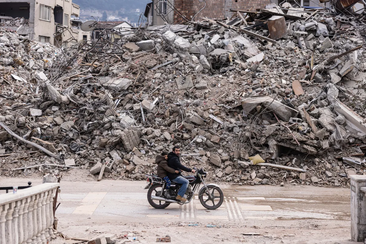 A man rides his motorcycle past collapsed buildings in the city of Antakya on February 19, 2023. A 7.8-magnitude earthquake hit near Gaziantep, Turkey, in the early hours of February 6, followed by another 7.5-magnitude tremor just after midday. The quakes caused widespread destruction in southern Turkey and northern Syria and has killed more than 44,000 people. (Photo by Sameer Al-DOUMY / AFP)