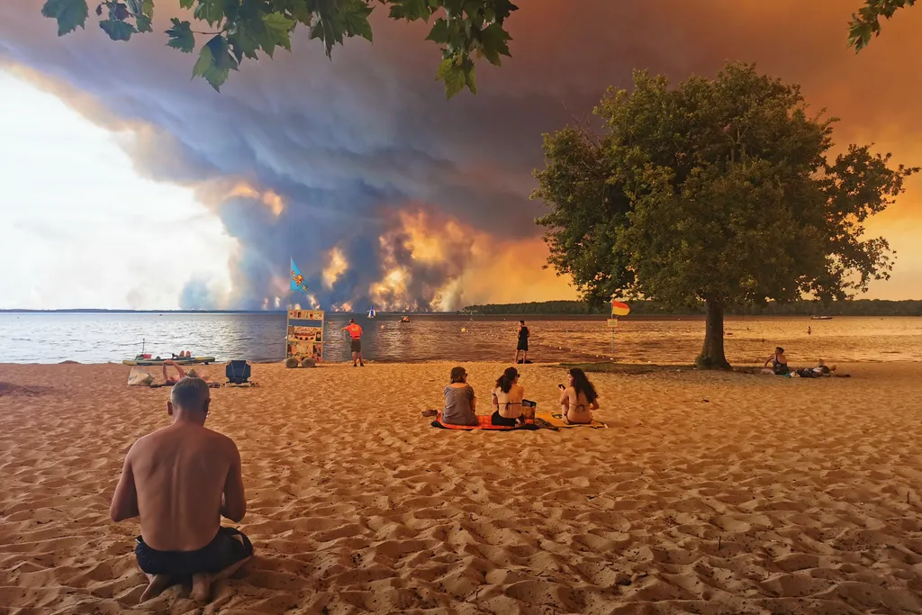 Beach goers rest on the beach of Moutchic on the shore of Lake Lacanau (Etang de Lacanau) in Lacanau , southwestern France on July 24, 2026, as clouds of smoke rise into the sky from the Gironde wildfire. The fire raging in the northern part of the Arcach