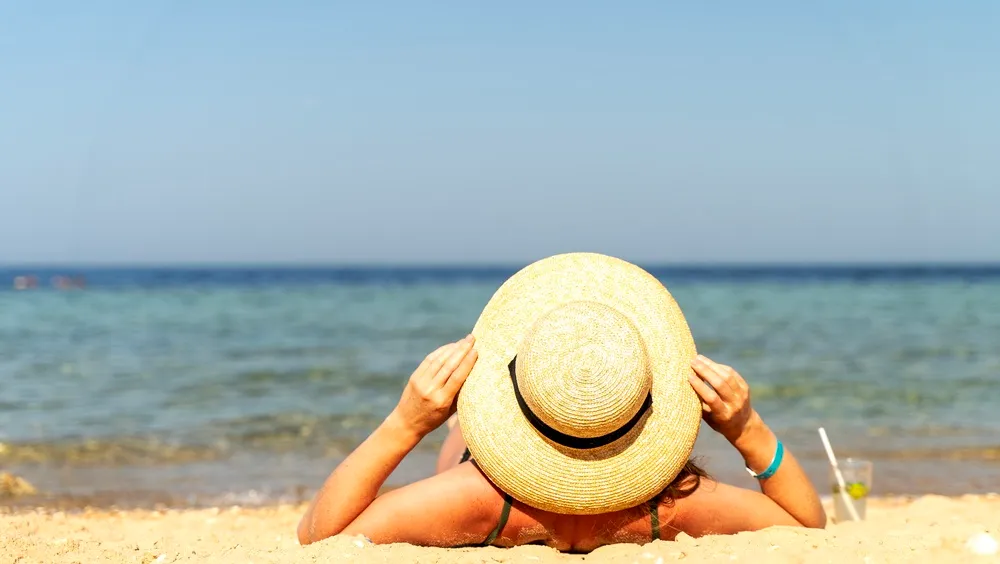 A napszúrás ellen világos szalmakalapot viselő nő a strandon