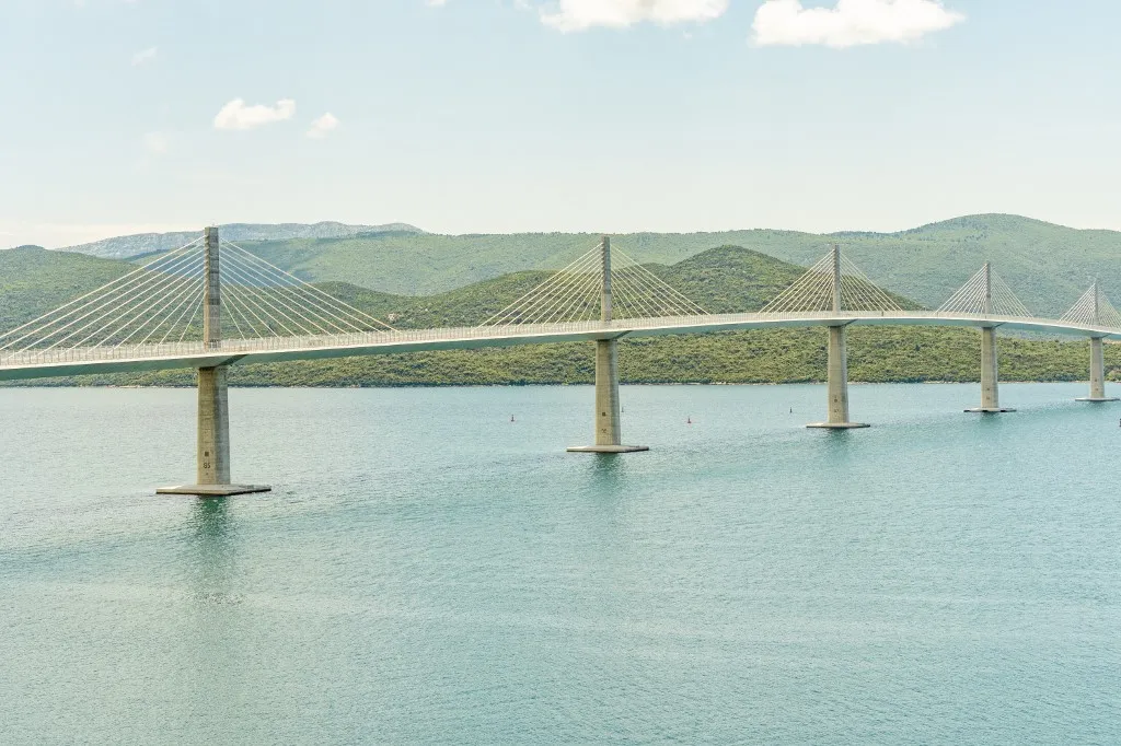 Coastal landscape featuring a long suspension Peljesac Bridge spanning across a blue bay with a lush green shoreline under a clear sky, Peljesac, Croatia (Photo by Armand Tamboly / Connect Images via AFP), Peljesac-híd