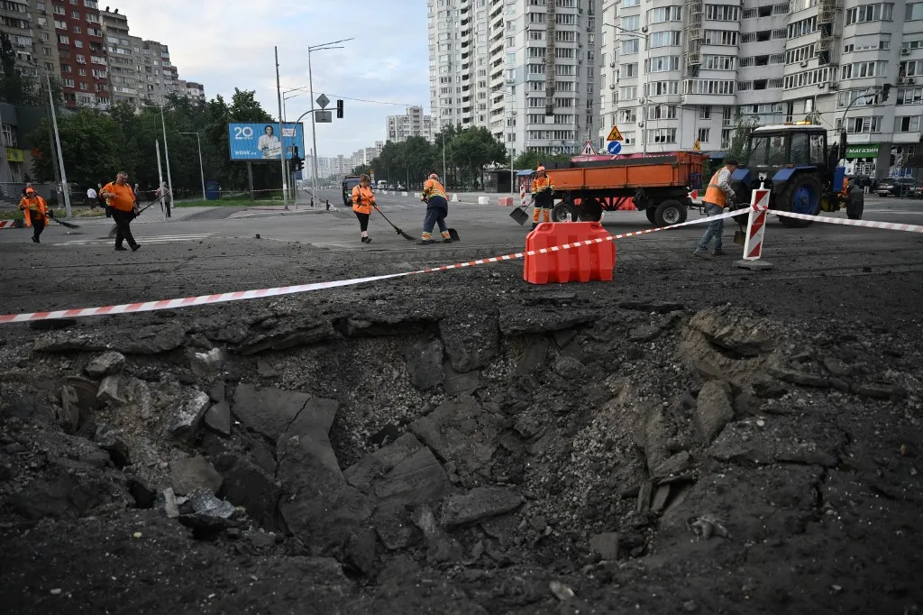 Communal workers clean around a crater from Russian missile strikes on the Ukrainian capital of Kyiv early on July 11, 2026, amid the Russian invasion in Ukraine. Ukraine said Russian missile strikes on Kyiv wounded six people, as Moscow escalates attacks on the Ukrainian capital. AFP journalists in Kyiv heard two series of explosions in the early hours of Saturday, with an air alert siren sounding minutes after the first blast. (Photo by Genya Savilov / AFP)