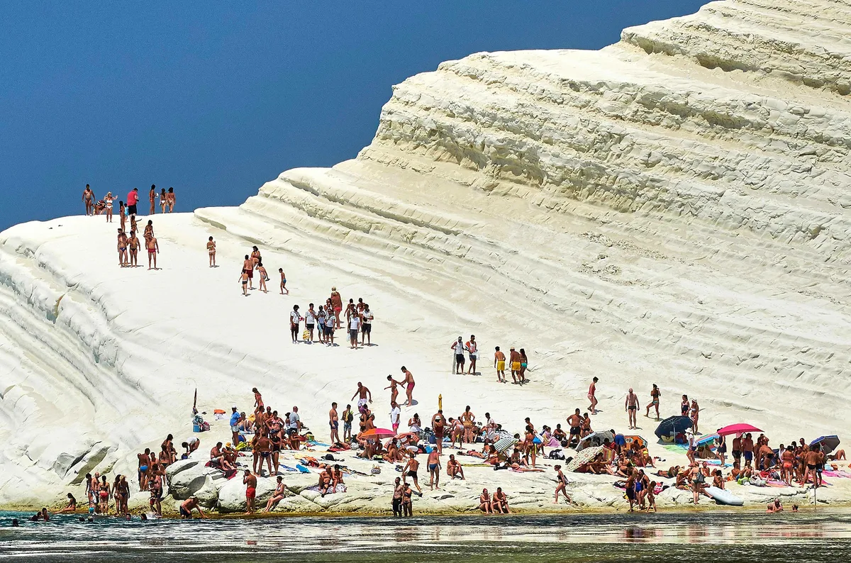 A Scala dei Turchi fehér mészkősziklái turistákkal, fürdőzőkkel. 