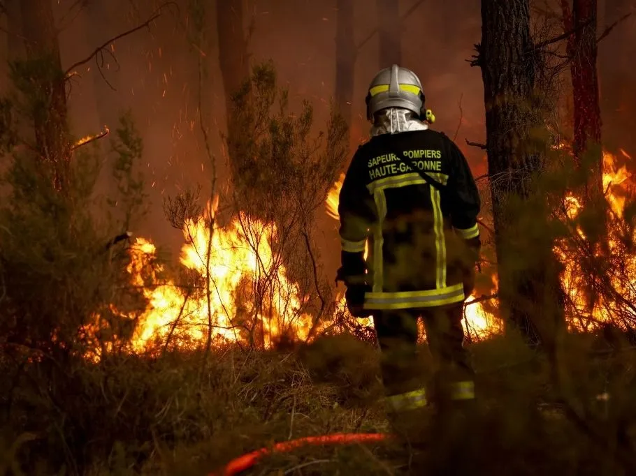 A firefighter stands before flames as a forest fire rages in Saint-Jean-d'Illac, some 30km from Bordeaux, on July 26, 2026 as a wildfire has been ravaging the forest north of the Arcachon Basin (Gironde). The 220,000 people evacuated due to the massive wildfire in France's Gironde region will not be able to return home "until the fire has been brought under control", the local prefect said, also ruling out any normal workday on Monday in the affected towns, ahead of a possible worsening of the situation on Tuesday due to an expected rise in temperatures. (Photo by ROMAIN PERROCHEAU / AFP)