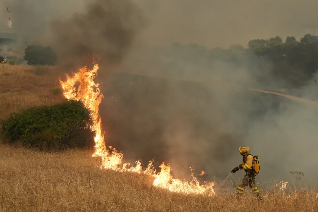 Firefighters battle a wildfire as a helicopter(L) dumps water on a wildfire in Cebreros area, near Avila, 80 kms west of Madrid on July 24, 2026. Spain declared a national emergency in the Madrid region and in the province of Avila, near the capital, on J