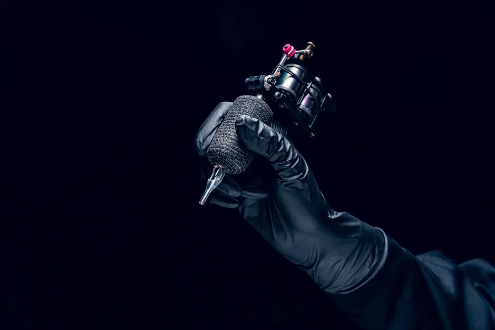 tetoválás, Machine for tattoo. Human hand in black protective glove holding professional equipment for making tattoo on body isolated on dark background. Concept of art, job, hobby, poster for ad