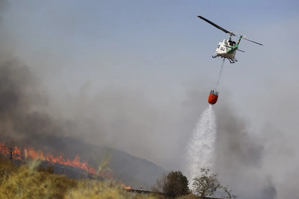ALMERIA, SPAIN - JULY 10: A firefighting helicopter releases its water load over heavy smoke during emergency operations to contain a massive wildfire while evacuation and firefighting efforts continue in the Los Gallardos district of Almeria, Spain on July 10, 2026. At least 12 people were killed in a forest fire that broke out Thursday in Los Gallardos municipality in Almeria province in Spain’s southern Andalusia region, broadcaster RTVE reported. According to Andalusia’s emergency services, the victims were found in a hamlet of the neighboring municipality of Bedar, with some discovered inside vehicles engulfed by the flames. Pablo Miranzo / Anadolu (Photo by Pablo Miranzo / Anadolu via AFP)