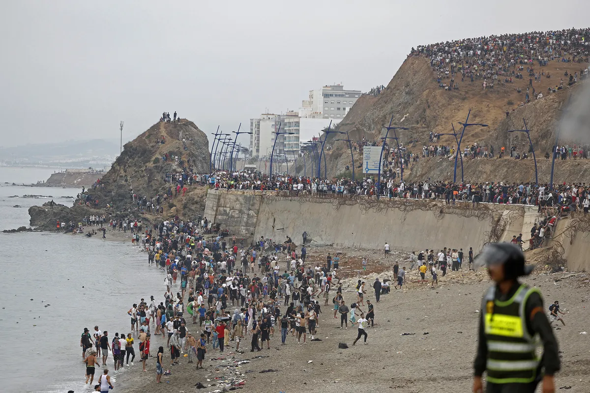 People gather along the fence at the site of clashes near Fnideq, on the Morocco-Spain border, on July 31, 2026. Thousands of migrants crossed overnight from Morocco into Spain's north Africa's Ceuta enclave, a police source said on July 31, as Prime Minister Pedro Sanchez was set to arrive to manage the latest migrant crisis on the border. (Photo by Abdel Majid BZIOUAT / AFP)