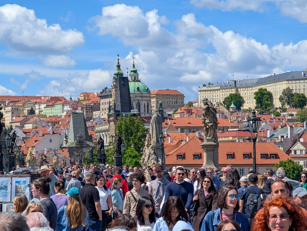 A dense crowd of tourists fills Charles Bridge under bright skies in Prague, Czech Republic, on May 11, 2025. Surrounded by historic statues and baroque towers, the bridge experiences extreme foot traffic, illustrating the growing challenges of overtourism in one of Europe's most visited cities. (Photo by Michael Nguyen/NurPhoto) (Photo by Michael Nguyen / NurPhoto via AFP)