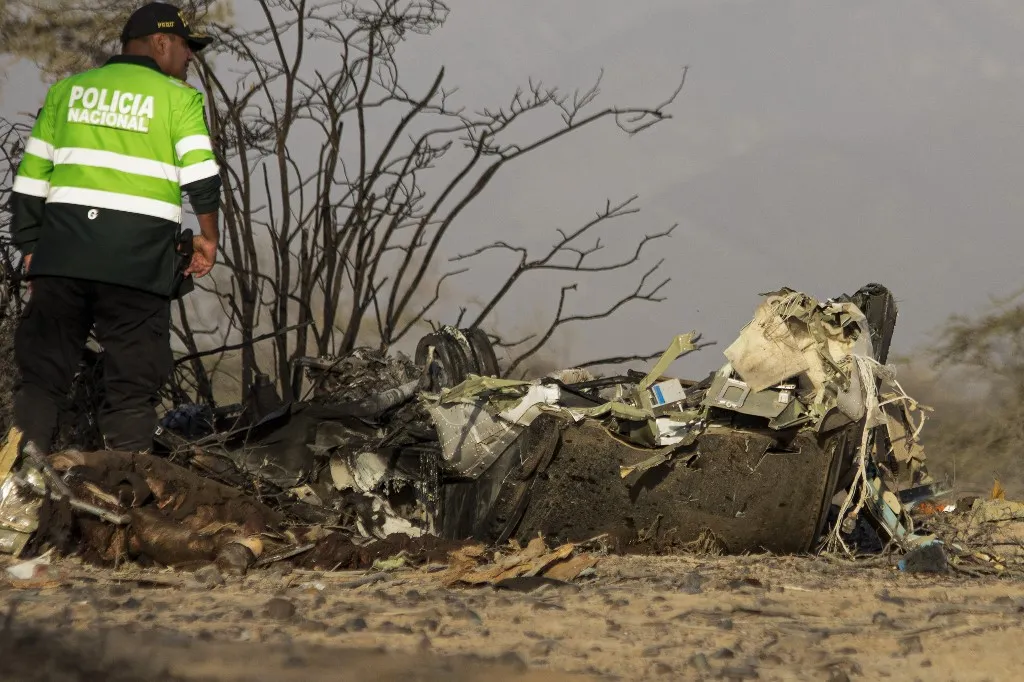 A police officer stands alongside the wreckage of the small plane involved in a fatal accident that claimed the lives of its 13 occupants in the Vista Alegre district, Nazca, Peru, on August 1, 2026. At least 13 people died when a small plane carrying tourists to see the ancient Nazca Linesone of Peru's archaeological attractionscrashed, police reported on August 1. (Photo by Mariajulia VAREMAN / AFP)