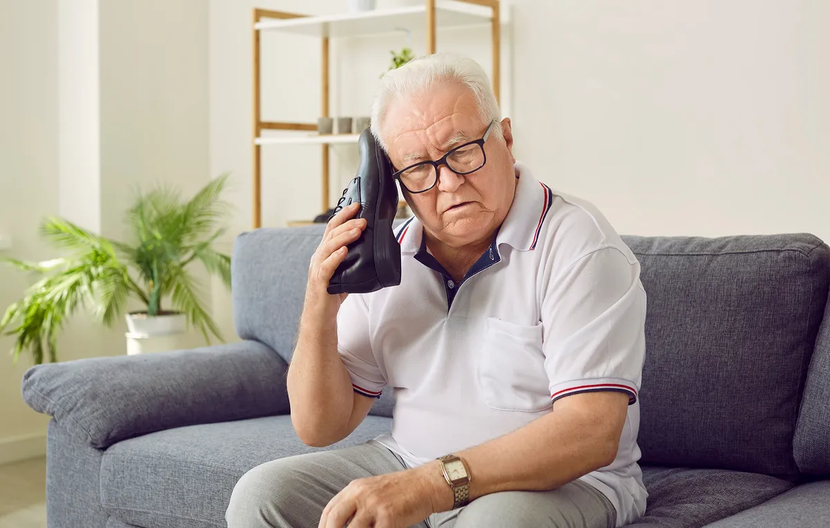 Alzheimer-kór betegségben szenvedő idős férfi egy cipővel próbál telefonálni.