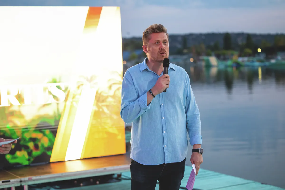 Fischer Gábor a TV2 programiazgatója kék ingben beszél a mkrofonba egy rendezvényen.