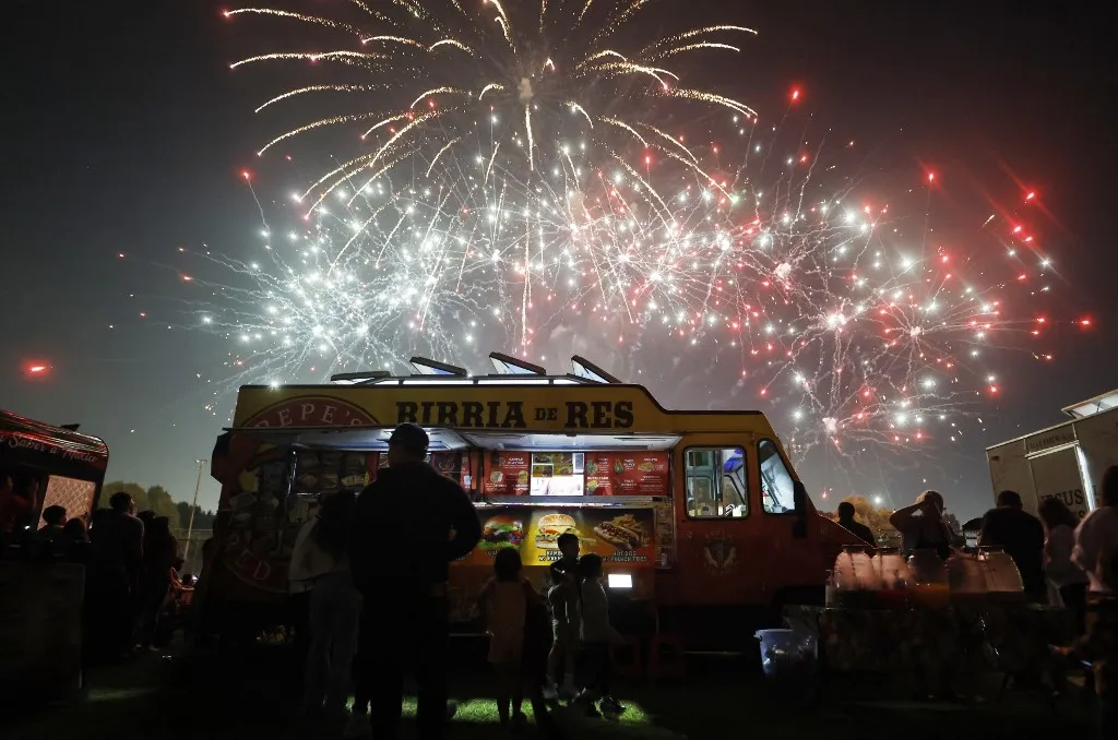 SOUTH GATE, CALIFORNIA - JULY 04: Fireworks explode as people gather by a food truck serving birria de res, a traditional Mexican dish, during the annual Independence Day Celebration in the predominantly Latino community of South Gate on July 4, 2026 in South Gate, California. The annual event was canceled last year due to safety concerns amid widespread ICE raids across Los Angeles County. People around the nation are celebrating America's 250th anniversary of the July 4th signing of the Declaration of Independence today. Mario Tama/Getty Images/AFP (Photo by MARIO TAMA / GETTY IMAGES NORTH AMERICA / Getty Images via AFP), tűzijáték