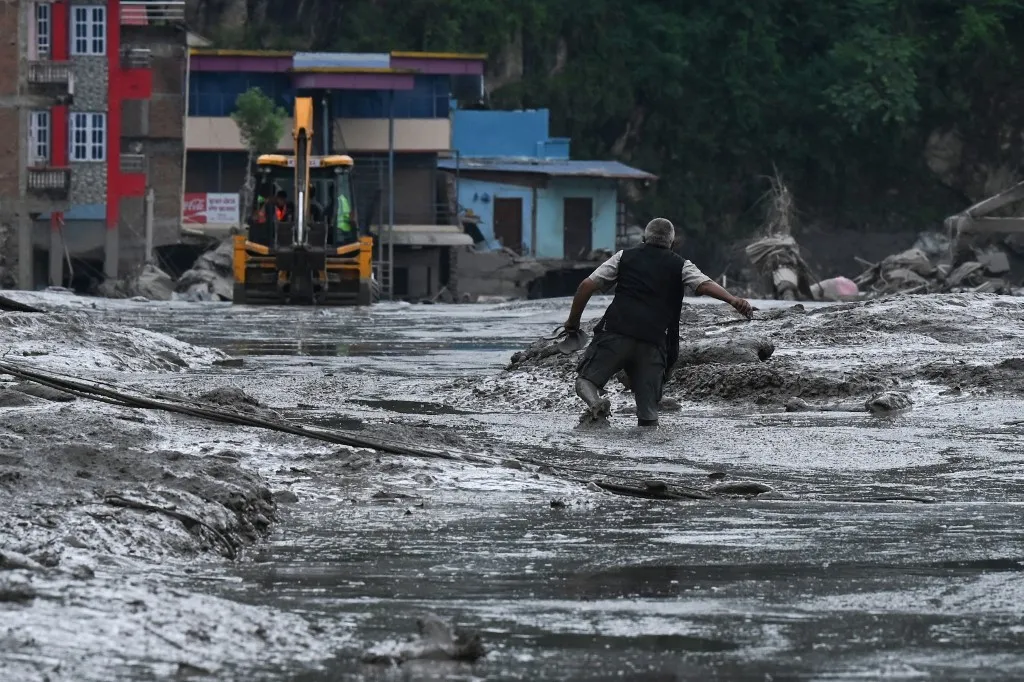 A resident walks along a street covered in mud following flash floods and a landslide disaster in Devighat, in Nepal's Nuwakot district on August 26, 2026. Rescue teams rushed on August 27 to find hundreds of people missing on the Nepal-Tibet border in flash floods and landslides that killed at least 160 and swept away entire villages. (Photo by PRAKASH MATHEMA / AFP)