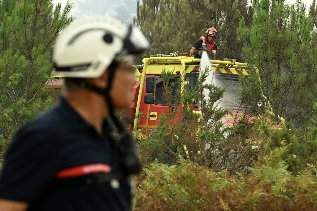 A helyszínen dolgozó tűzoltók A firefighter douses water over trees during a wildfire in a forest near Luglon, south-western France on August 15, 2026. Firefighters focused on August 15, 2026, their efforts, both from the air and on the ground, on a flare-up that occurred at dawn in the Landes forest, taking advantage of cooler temperatures to try to contain the blaze, which has already consumed nearly 1,600 hectares. Around 550 firefighters are battling this third major summer blaze in the vast Landes de Gascogne forest, an area dominated by maritime pines parched by heatwaves driven by climate change, following the fires that broke out in late July at Biscarrosse (Landes, 3,700 hectares) and Saumos (Gironde, 42,000 hectares). (Photo by Gaizka IROZ / AFP)