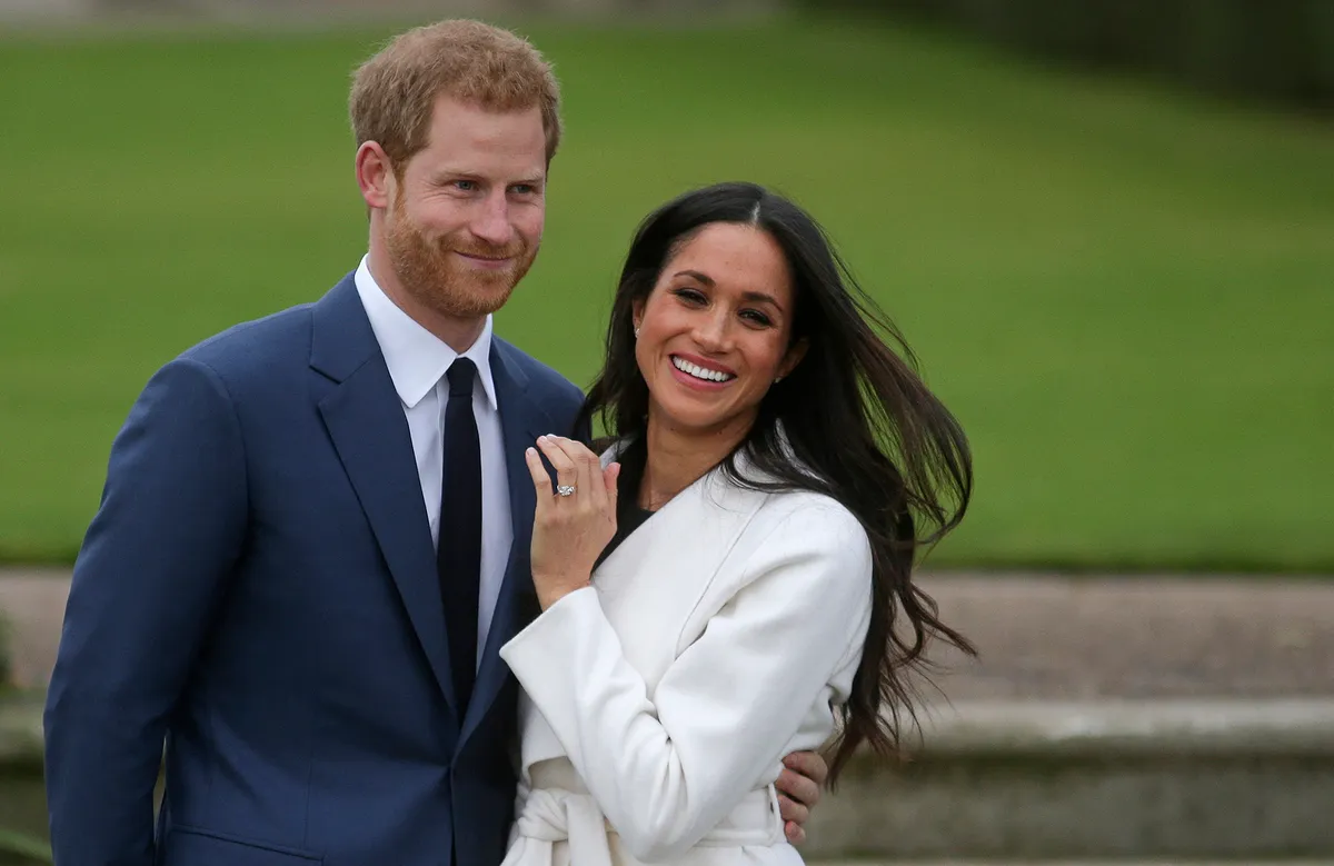 Britain's Prince Harry stands with his fiancée US actress Meghan Markle as she shows off her engagement ring whilst they pose for a photograph in the Sunken Garden at Kensington Palace in west London on November 27, 2017, following the announcement of their engagement. Britain's Prince Harry will marry his US actress girlfriend Meghan Markle early next year after the couple became engaged earlier this month, Clarence House announced on Monday. (Photo by Daniel LEAL / AFP)