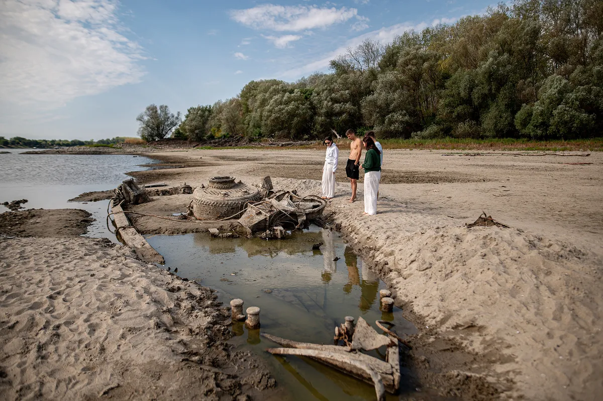 BAJA, HUNGARY â€“ AUGUST 8: People gather along the exposed riverbed of the Danube, after exceptionally low water levels revealed the remains of an old World War II-era ship from the riverbed in Baja, Hungary on August 8, 2026. The emergence of the wreck has attracted hundreds of curious visitors to the site. Robert Nemeti / Anadolu (Photo by Robert Nemeti / Anadolu via AFP)