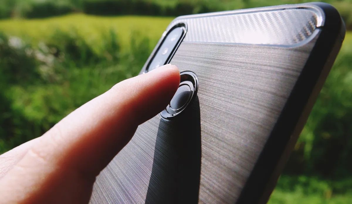 The hand is holding a black phone and the index finger is touching the fingerprint scanner to unlock the smartphone