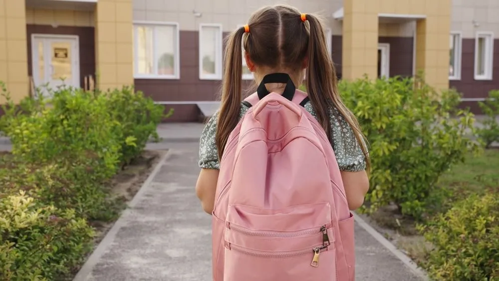 Kislány hátizsákkal ál az iskola előtt az iskolakezdés napján