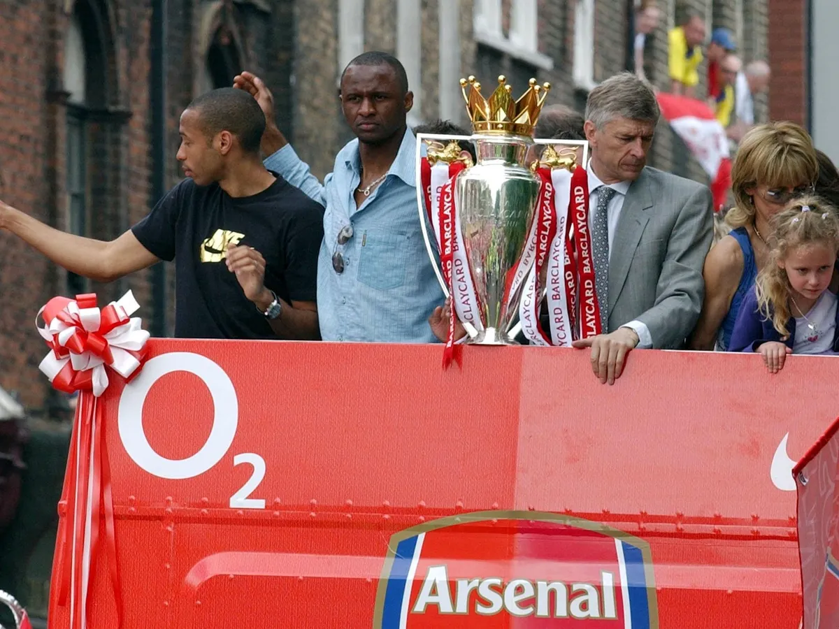 Arsenal's Thierry Henry (L), captain Patrick Vieira (2ndL) and manager Arsen Venger are pictured on the open-top bus carrying the winners of the British Premier League Championship, Arsenal players and their families, on their way to Islington Town Hall, 16 May 2004, as part of the Club's victory celebration.  AFP PHOTO/ Martyn HAYHOW (Photo by MARTIN HAYHOW / AFP)