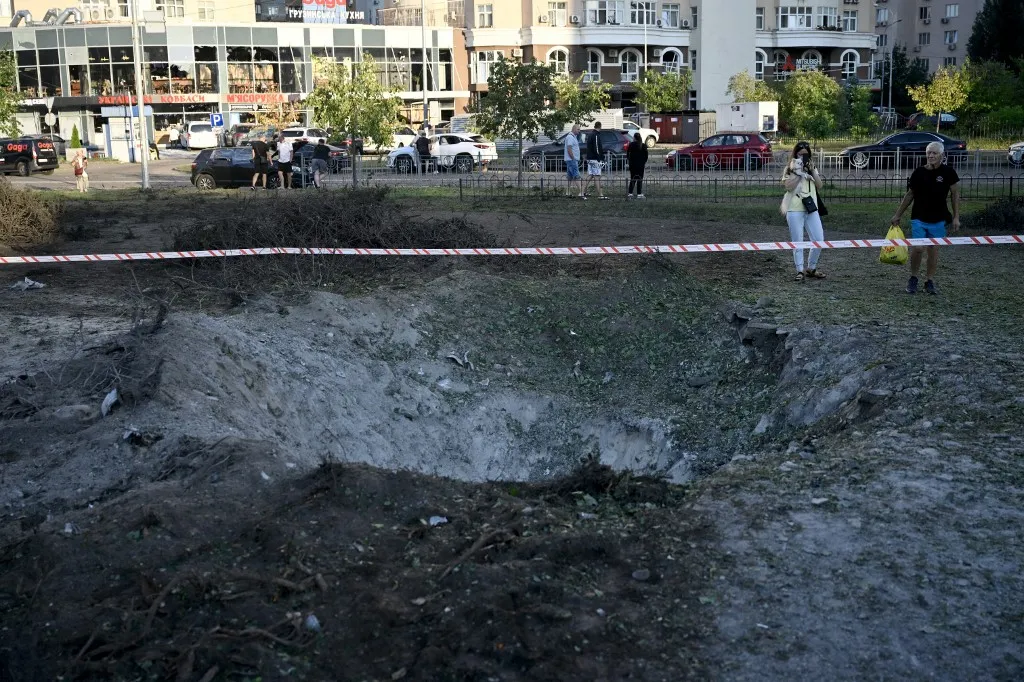 People examine a crater from Russian ballistic missile near children's clinic following massive Russian ballistic missile strikes in the Ukrainian capital of Kyiv on August 1, 2026, amid the Russian invasion in Ukraine. The death toll from Russian strikes on Kyiv has risen to nine, Ukraine's emergency service said. (Photo by Genya Savilov / AFP), Ukrajna, Kijev, orosz rakétatámadás